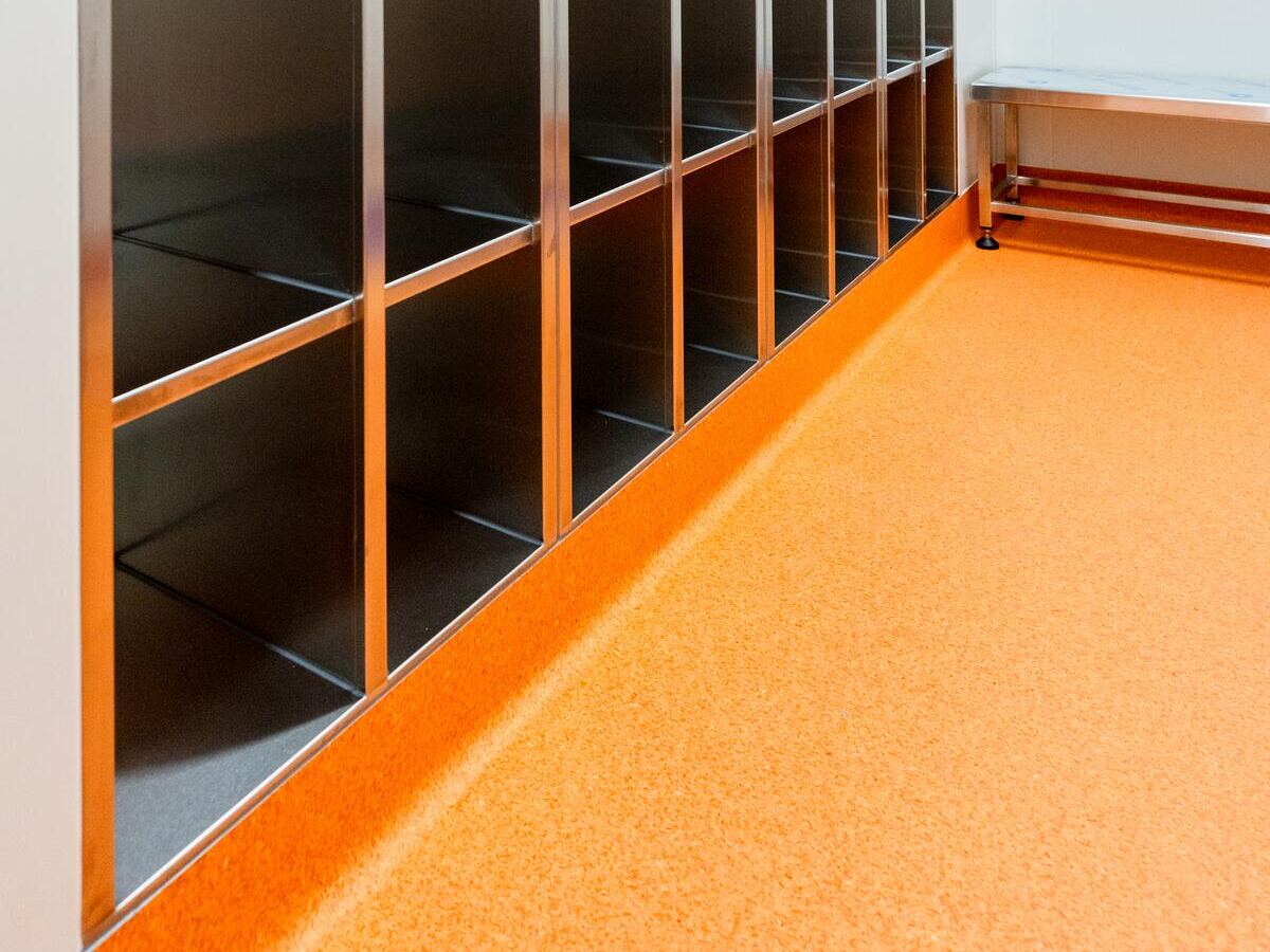 Orange coved vinyl beneath stainless shelving in a controlled room at PolyNovo, installed by JA Floors