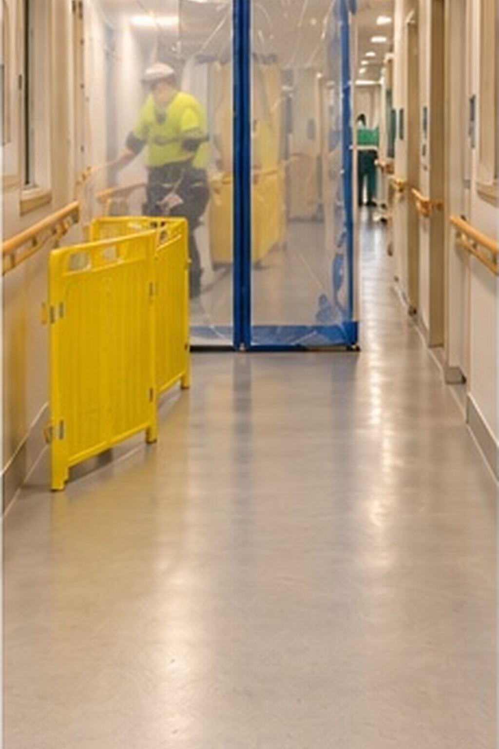 Corridor with handrails, a temporary plastic screen and a yellow barrier around a floor work area